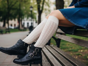 Žena sediaca na lavičke v parku s ponožkami po kolená a členkovými topánkami.